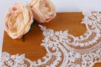 two delicate pink roses resting on a wooden surface, with a decorative white lace overlay in the foreground.