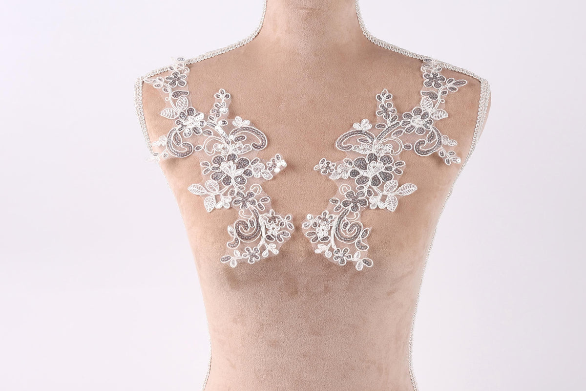A mannequin with two white floral lace pieces sewn onto its shoulders.