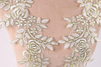 a close-up view of a delicate, intricate piece of embroidered fabric with a floral pattern. The fabric appears to be made of a soft, light-colored material, possibly cotton or a similar natural fiber. The embroidery is composed of numerous small, white flowers and leaves, arranged in a symmetrical and visually appealing manner. The overall composition of the image is focused on the intricate details and craftsmanship of the embroidered fabric.