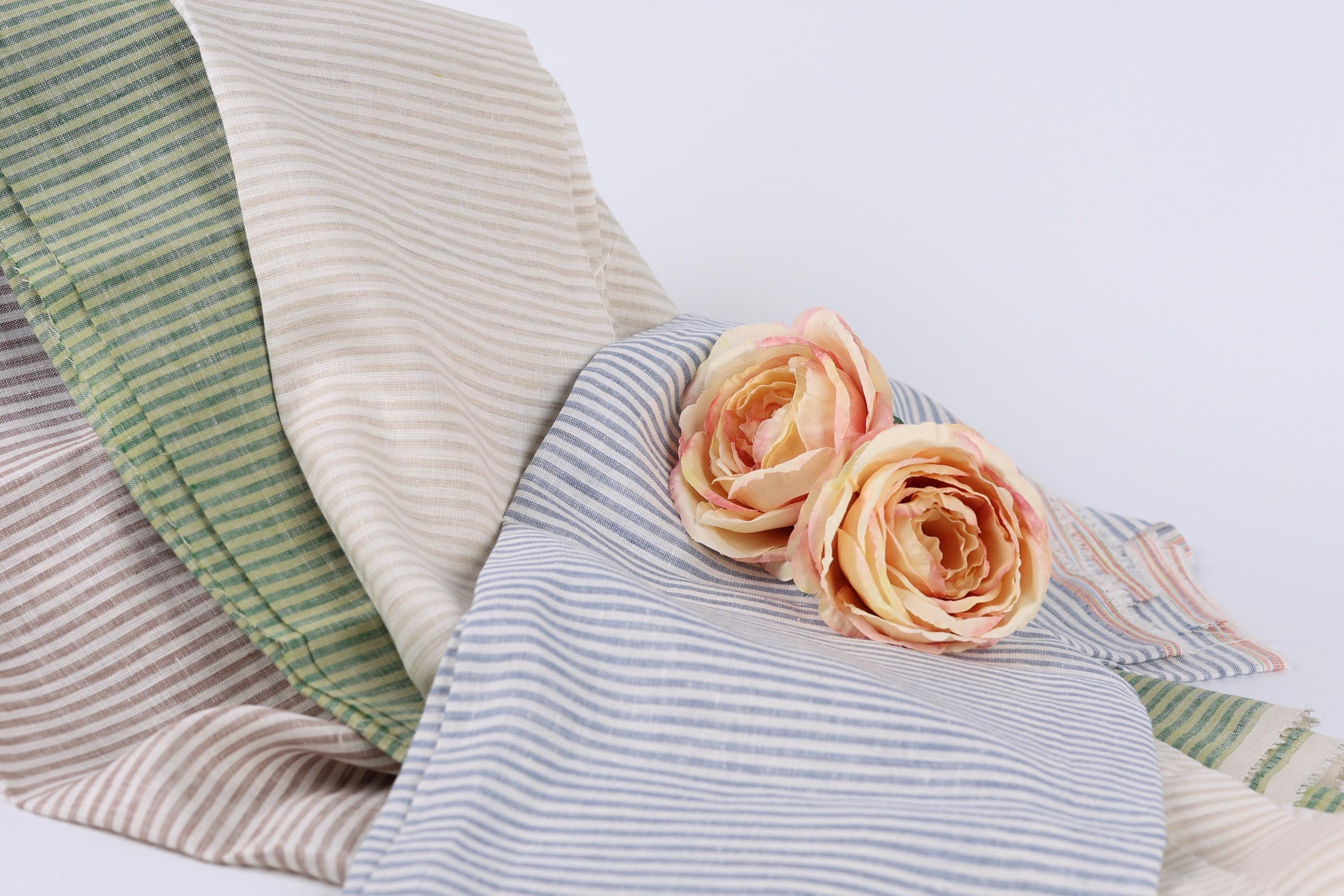 two pink roses resting on a blue and white striped fabric.