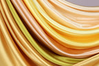 a close-up view of a fabric with a vibrant, multicolored pattern. The fabric appears to be made of silk or satin, with a smooth and shiny texture. The colors of the fabric are a mix of yellow, orange, and green, creating a visually striking and dynamic composition.