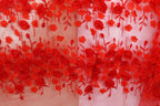 a close-up view of a fabric with a floral pattern of red roses and leaves. The fabric appears to be a sheer material, with the red flowers and leaves hanging down in a decorative manner.
