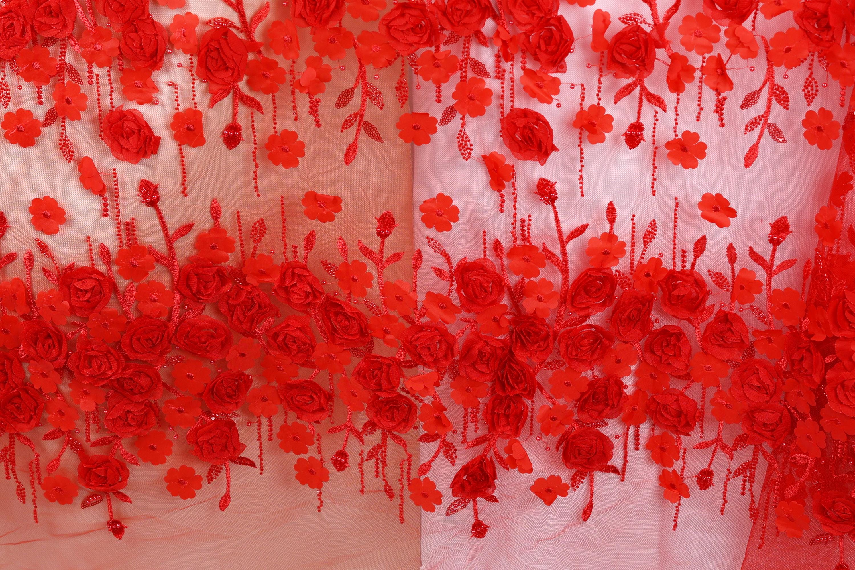 a close-up view of a fabric with a floral pattern of red roses and leaves. The fabric appears to be a sheer material, with the red flowers and leaves hanging down in a decorative manner.