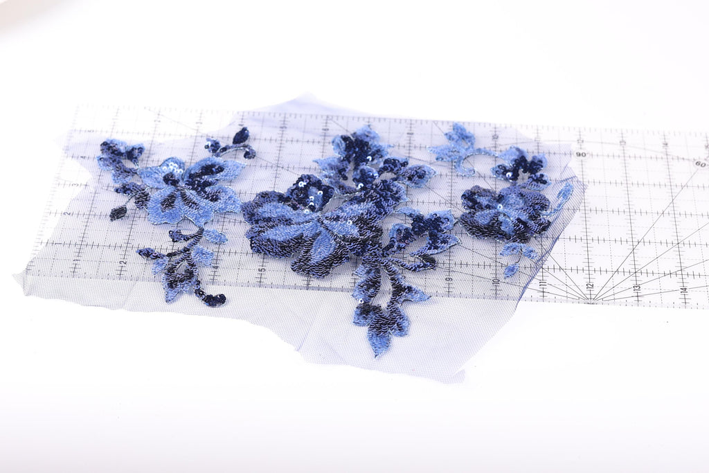 a piece of fabric with blue sequin flowers and leaves, placed on a transparent surface.