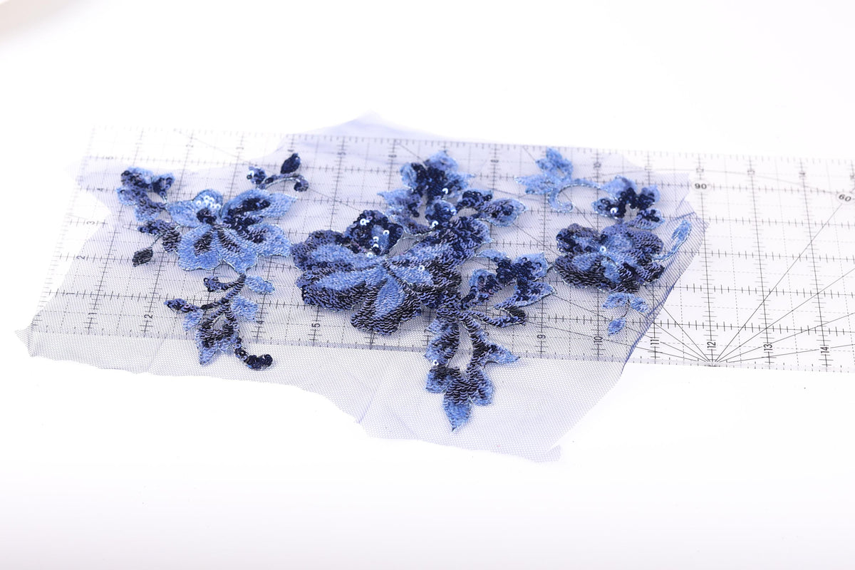 a piece of fabric with blue sequin flowers and leaves, placed on a transparent surface.