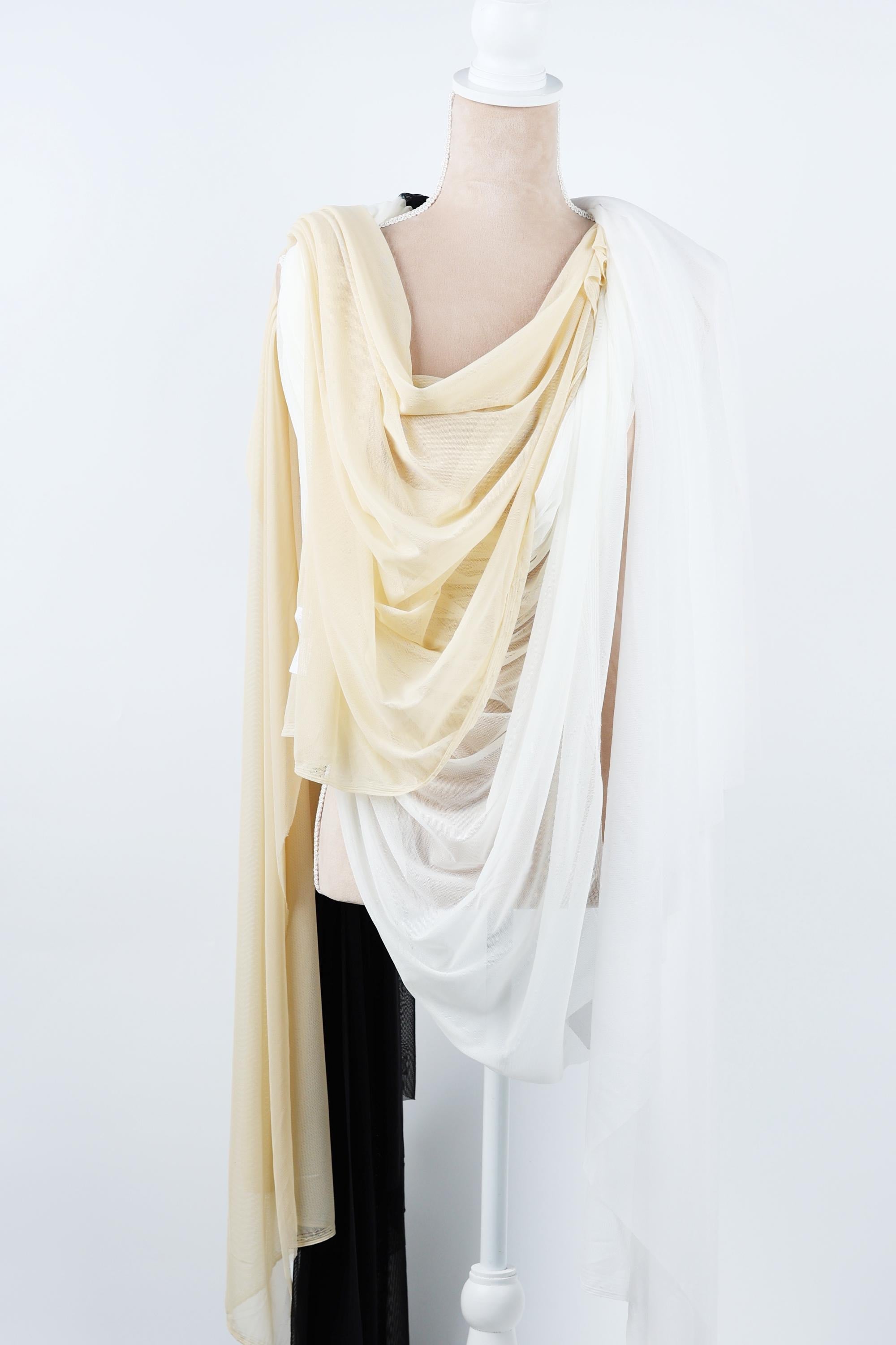A mannequin wearing a white dress with a draped, flowing yellow and white scarf draped over the shoulder.