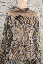 a mannequin wearing a dress with a sheer, sheer-like fabric that has a floral pattern. The dress appears to be made of sequins and has a black and gold color scheme.