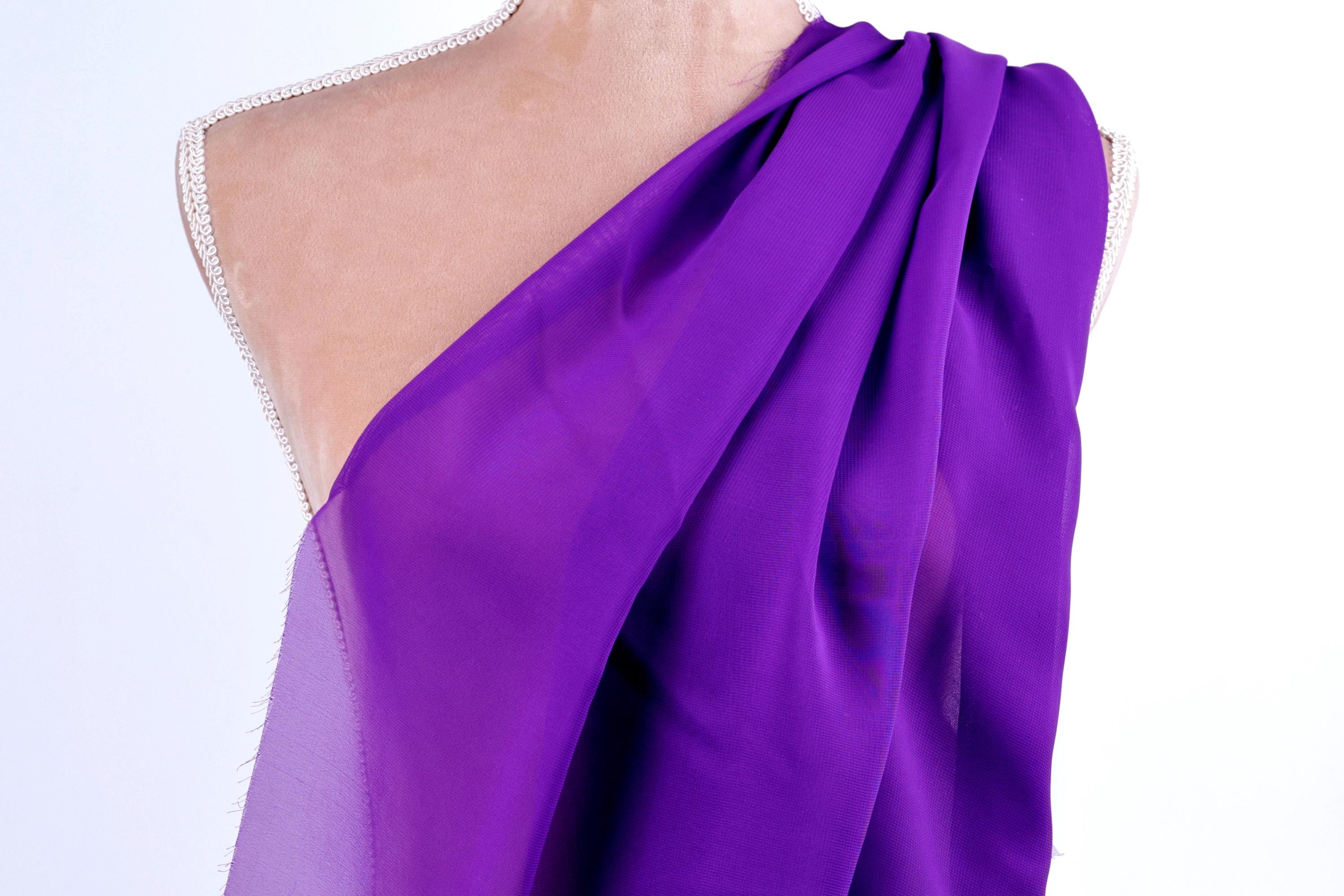 A mannequin wearing a purple draped fabric draped over its shoulder.