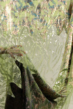 a close-up view of a fabric with a green and gold pattern, with a blurred background that appears to be a light green color.