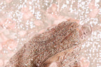 A close-up view of a delicate, intricately beaded fabric with a soft, pastel pink hue.