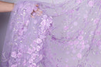 A close-up view of a delicate, hand-embroidered fabric with a floral pattern in shades of purple.