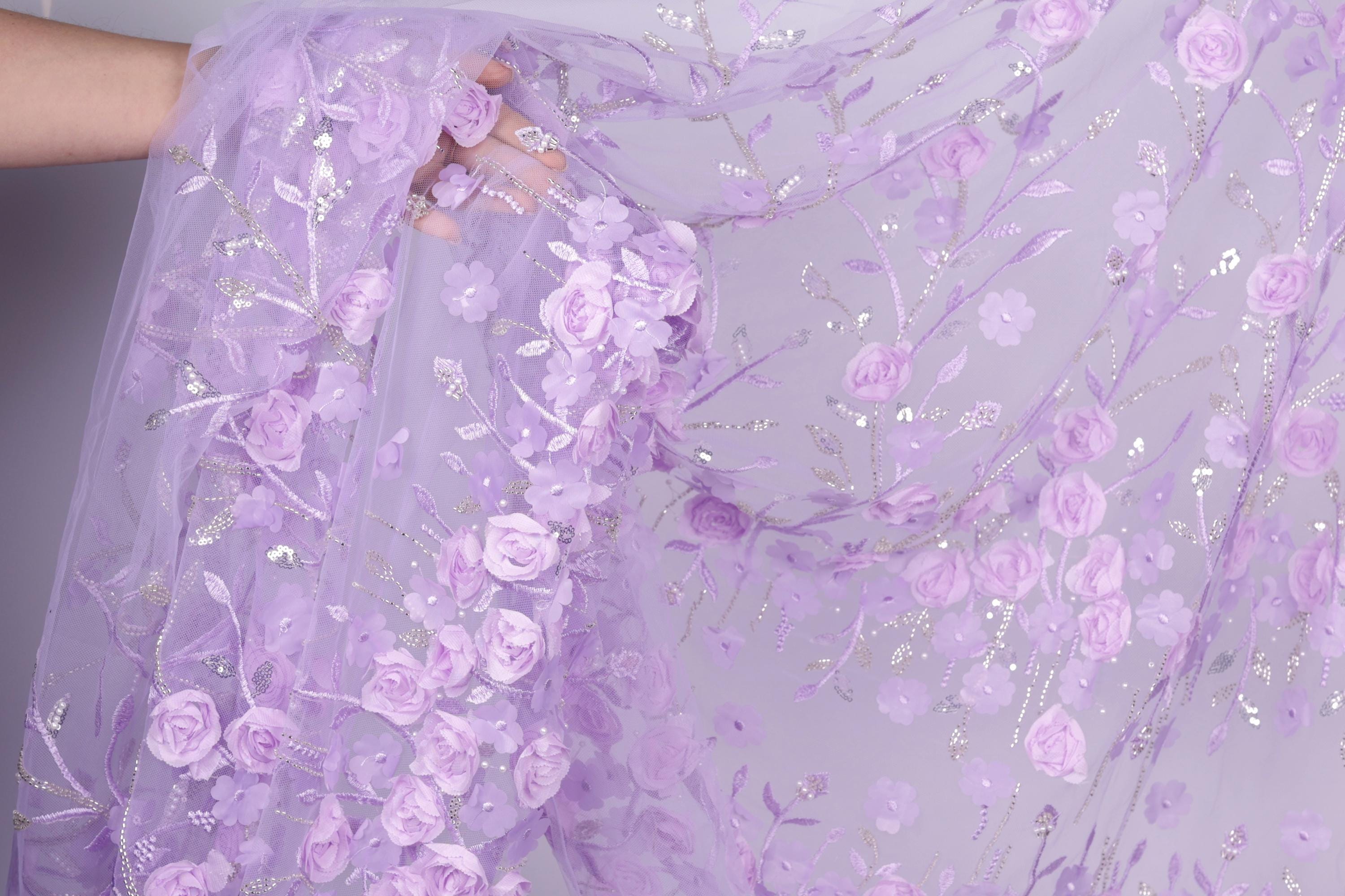 A close-up view of a delicate, hand-embroidered fabric with a floral pattern in shades of purple.