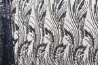 a close-up view of a fabric with a repeating pattern of black and white lines and shapes, resembling a floral or leaf-like design.