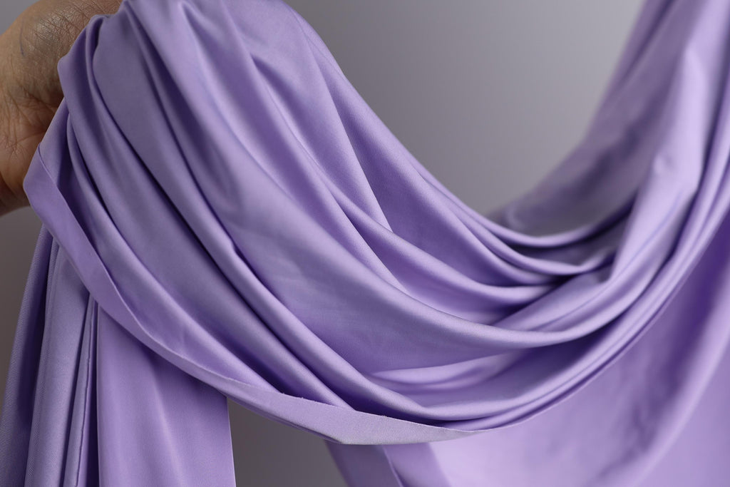 A hand is holding a piece of lavender fabric, which appears to be a soft, flowing material.