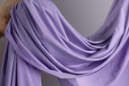 A hand is holding a piece of lavender fabric, which appears to be a soft, flowing material.