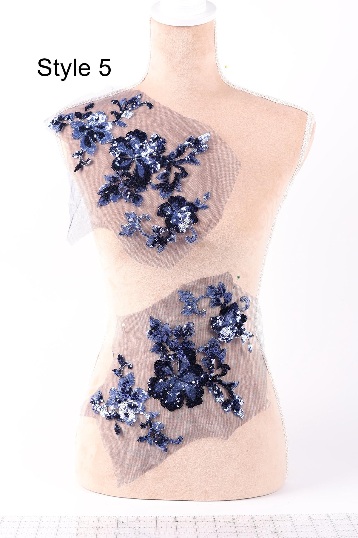 A mannequin with a beige body and a white head, wearing a dress with blue floral embroidery.