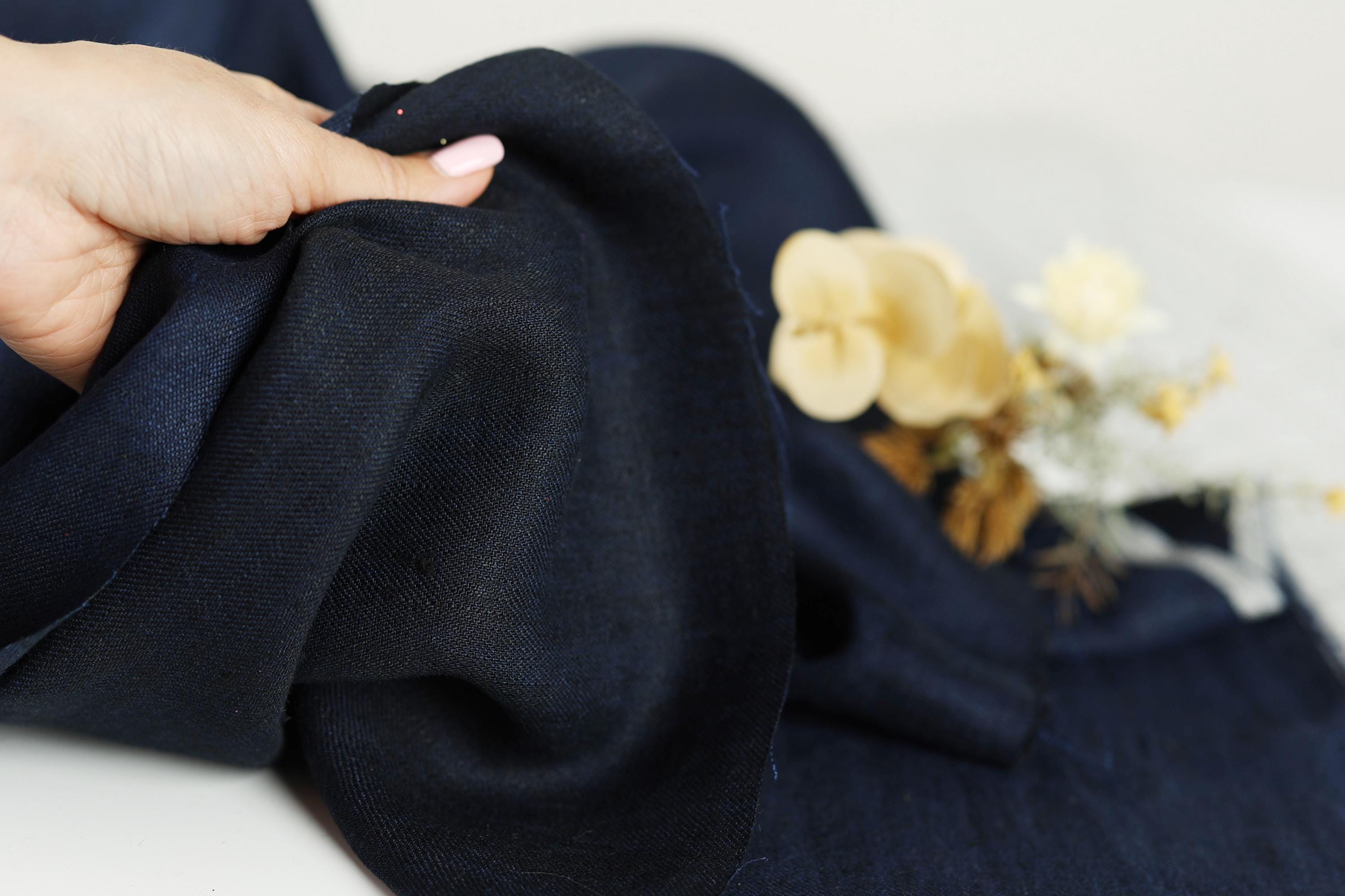 A hand is holding a piece of dark blue fabric, with a small bouquet of yellow flowers visible in the background.