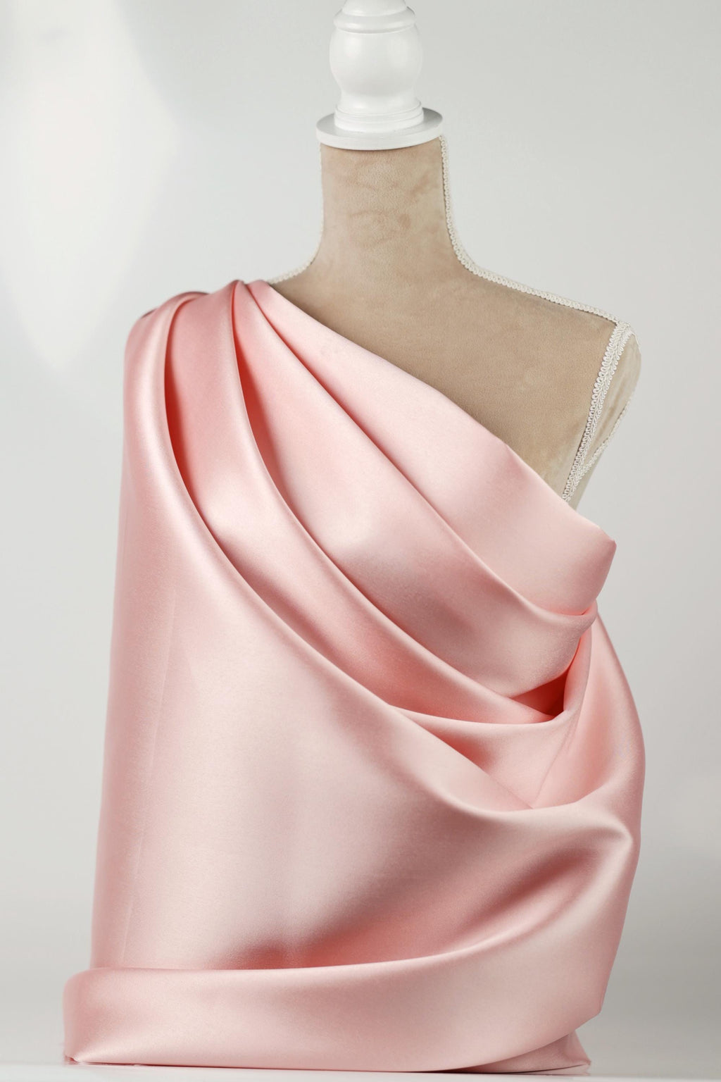 A mannequin wearing a pink satin dress with a draped, flowing silhouette.