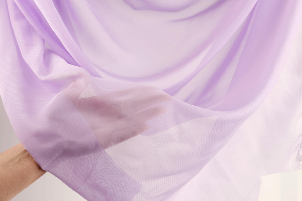 A hand is holding a piece of lavender fabric, which appears to be a soft, flowing material.