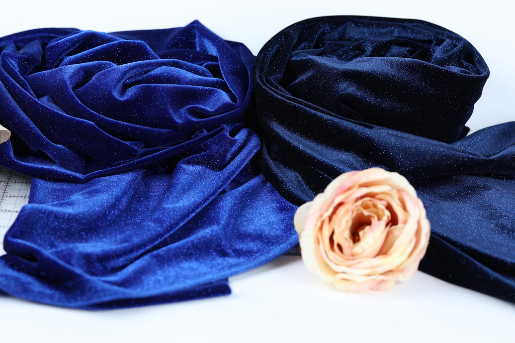 a close-up view of a pink rose resting on a white surface, surrounded by various blue and black fabric materials.