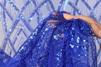 A hand is holding a piece of blue sequin fabric, which appears to be a decorative textile.