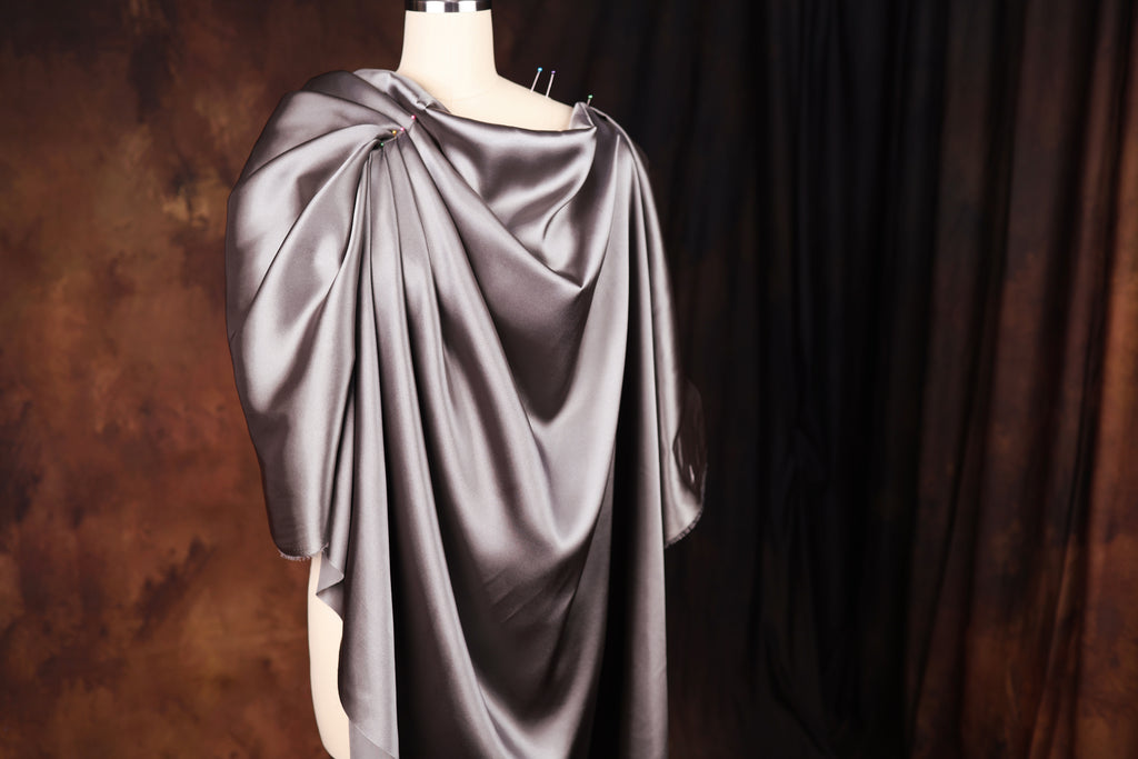 A mannequin wearing a gray satin cape with a draped, flowing design.