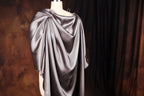 A mannequin wearing a gray satin cape with a draped, flowing design.