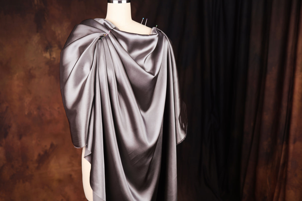 A mannequin wearing a gray satin cape with a draped, flowing design.