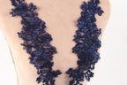 a close-up view of a mannequin torso wearing a dress with a floral lace overlay. The lace is intricately designed and appears to be made of a dark blue material, creating a striking contrast against the light-colored fabric of the dress.