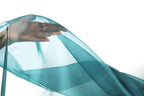 A hand is holding a piece of blue fabric, which appears to be a sheer or sheer-like material, against a white background.