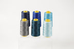 six spools of thread in various colors, including blue, gray, and turquoise, arranged in a neat row on a white background.