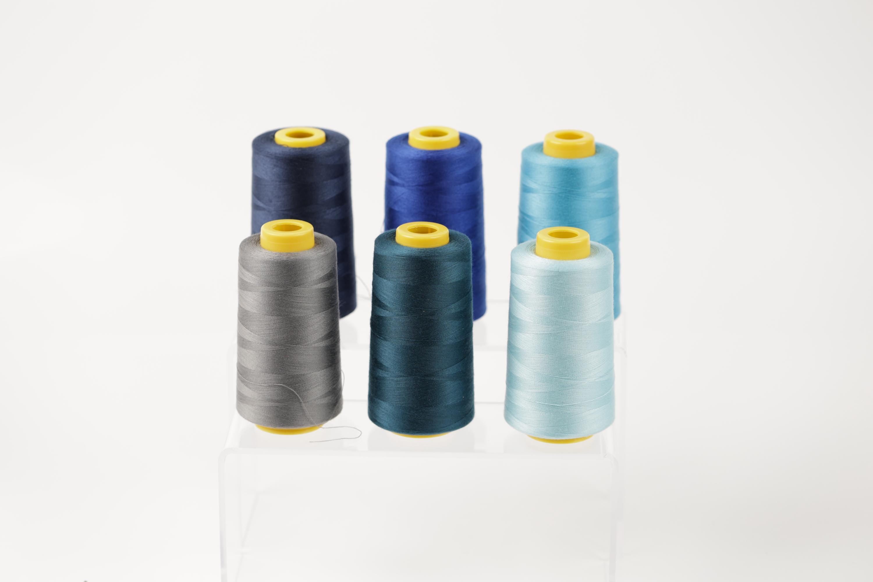 six spools of thread in various colors, including blue, gray, and turquoise, arranged in a neat row on a white background.