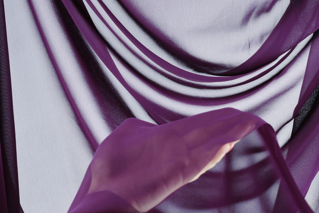 a hand holding a purple fabric, with the fabric appearing to be made of a soft, flowing material.