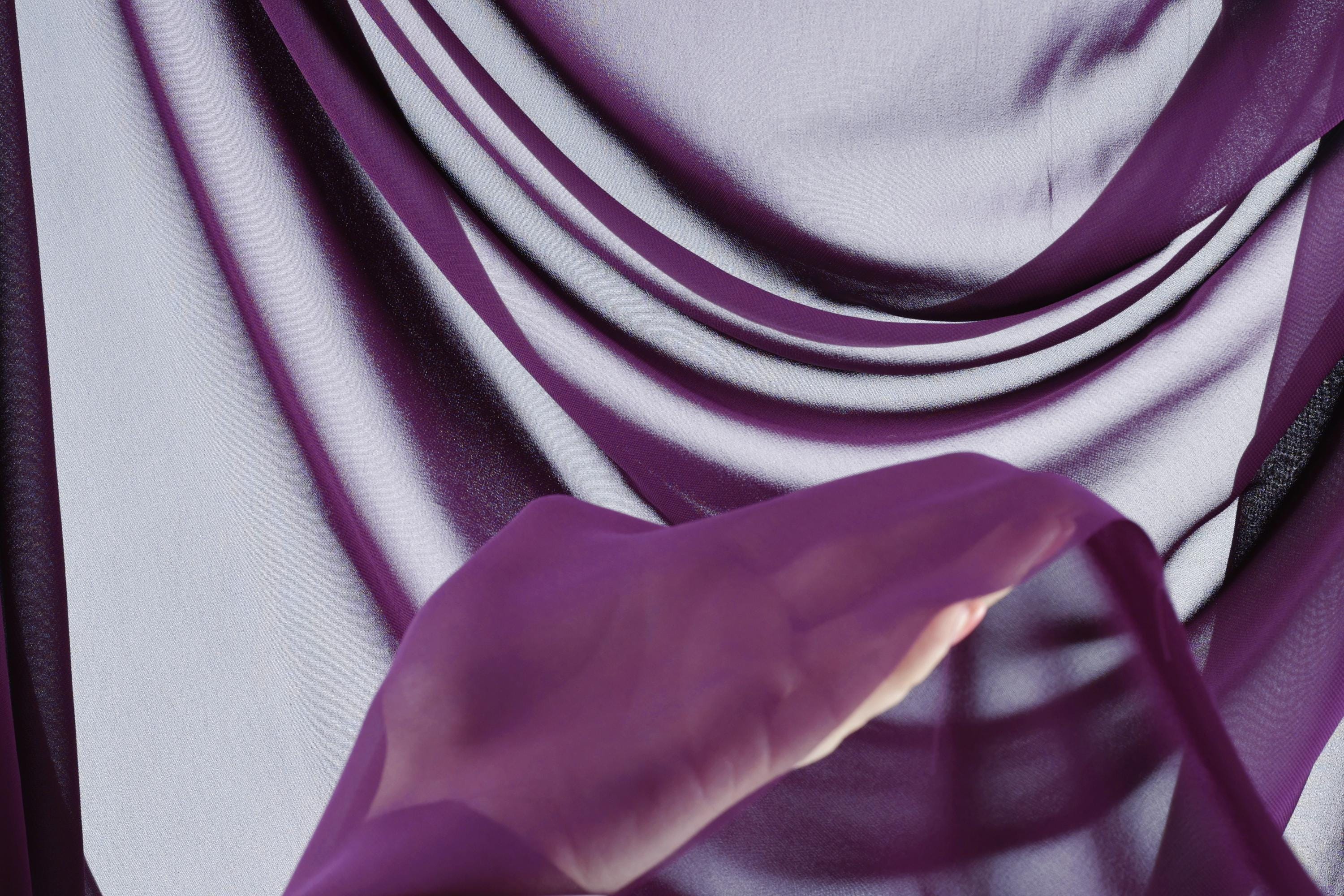 a hand holding a purple fabric, with the fabric appearing to be made of a soft, flowing material.