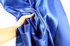 A hand is holding a piece of blue satin fabric, which appears to be a close-up view of the material.