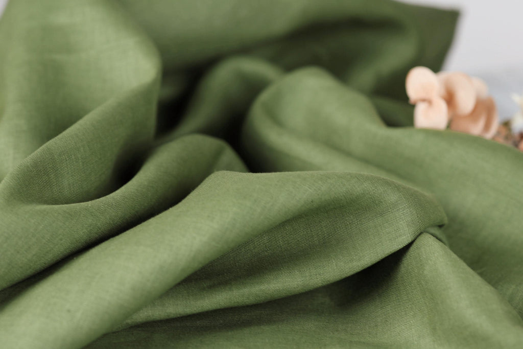 A close-up view of a crumpled, green fabric with a small, delicate flower resting on it.