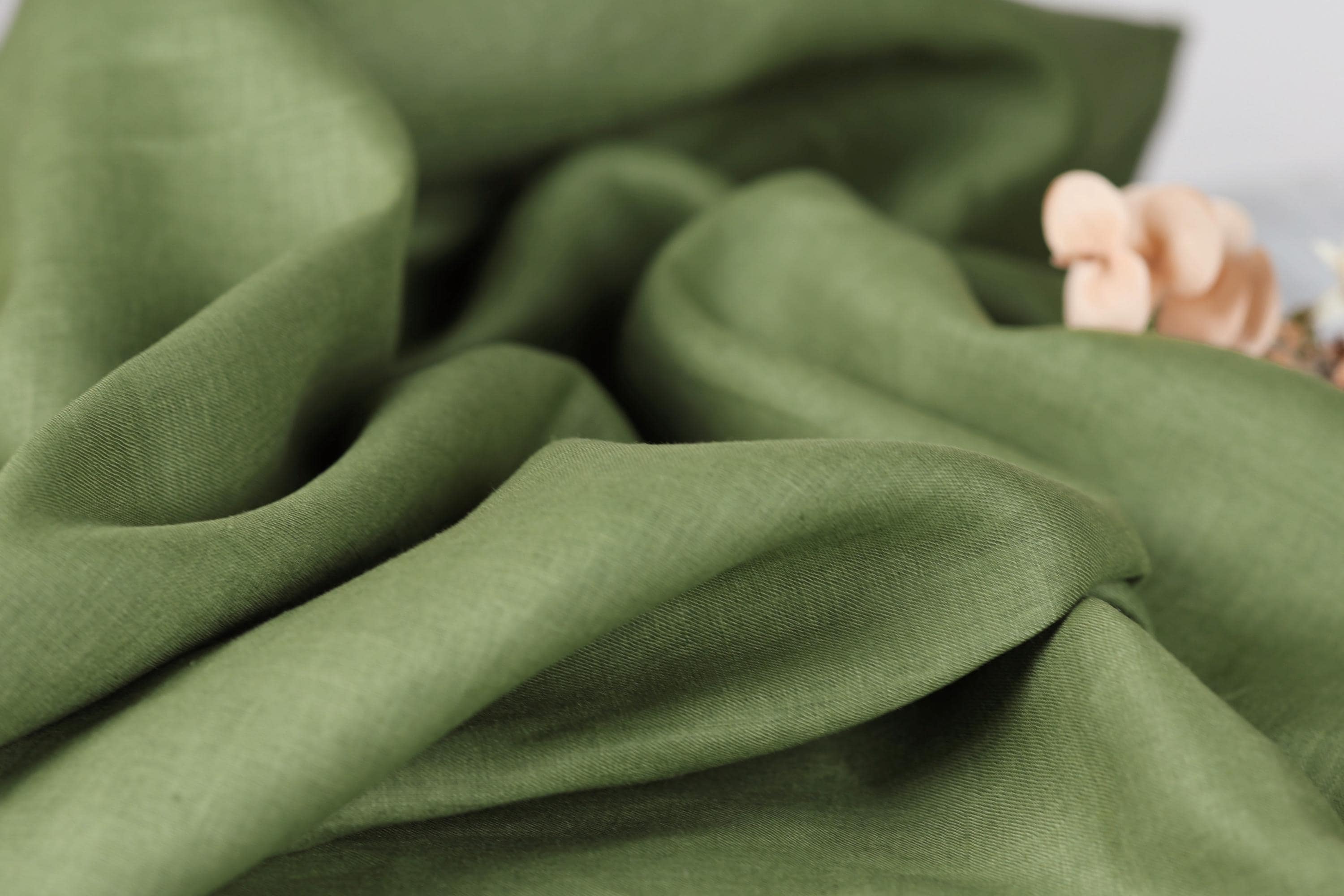 A close-up view of a crumpled, green fabric with a small, delicate flower resting on it.