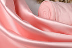A close-up view of a soft, pink satin fabric, with a rolled-up piece of the fabric visible in the background.