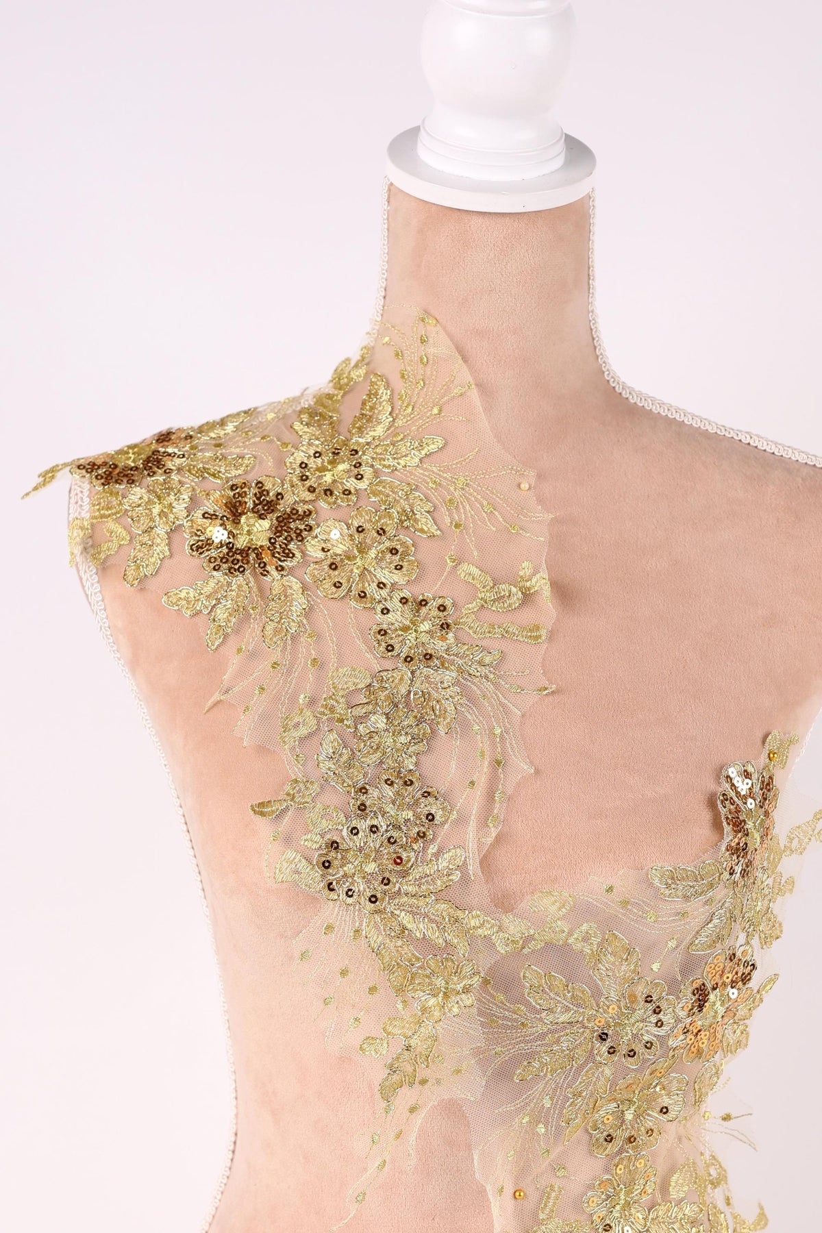 A mannequin wearing a dress with intricate gold and beige embroidered details, including flowers and leaves, creating a visually striking and elegant design.