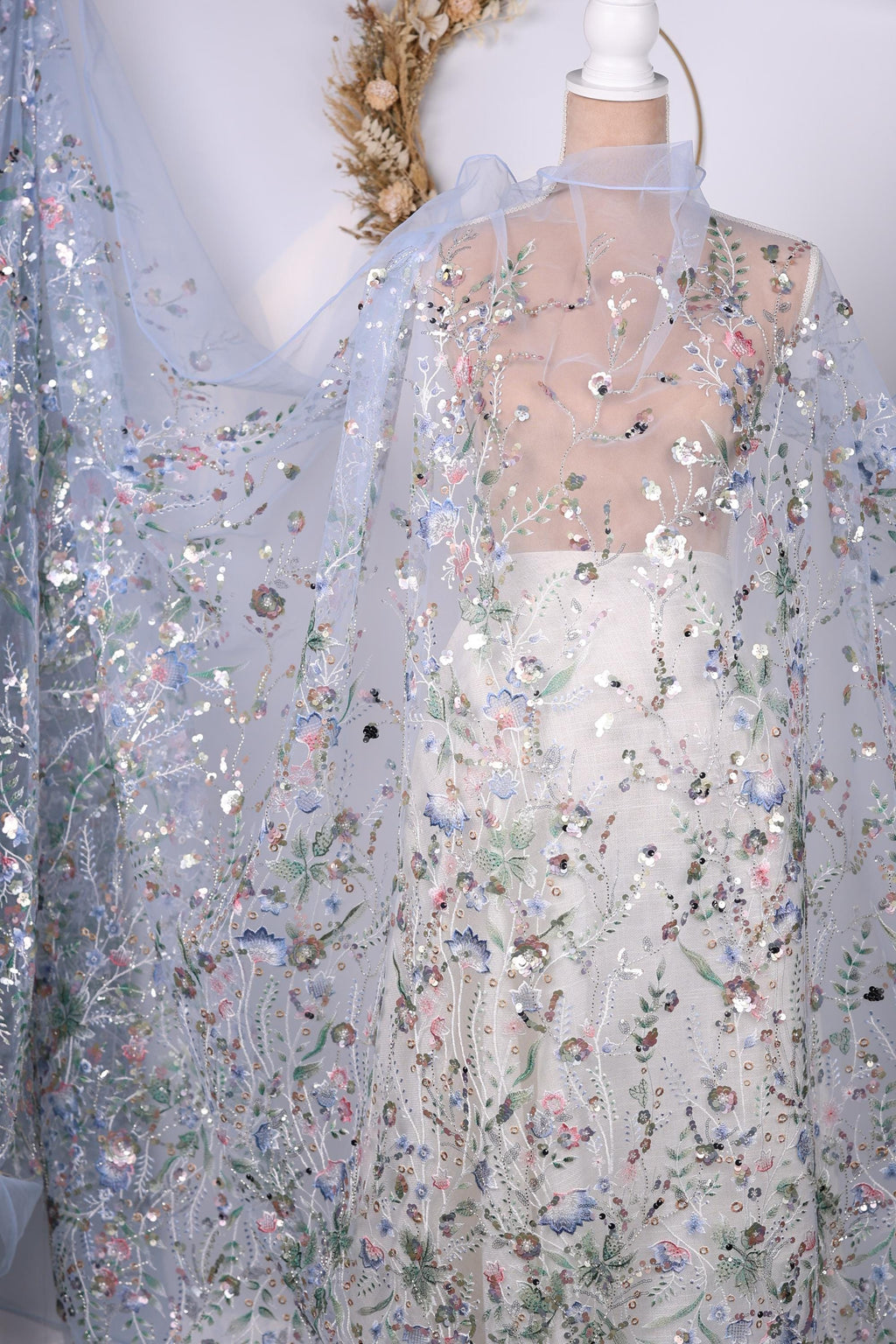 a delicate, intricately embroidered fabric with a floral pattern. The fabric appears to be a sheer material, with a light blue color and a floral design that adds a touch of elegance and sophistication to the piece. The fabric is displayed on a mannequin, showcasing its beauty and the craftsmanship involved in its creation.