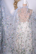 a delicate, intricately embroidered fabric with a floral pattern. The fabric appears to be a sheer material, with a light blue color and a floral design that adds a touch of elegance and sophistication to the piece. The fabric is displayed on a mannequin, showcasing its beauty and the craftsmanship involved in its creation.