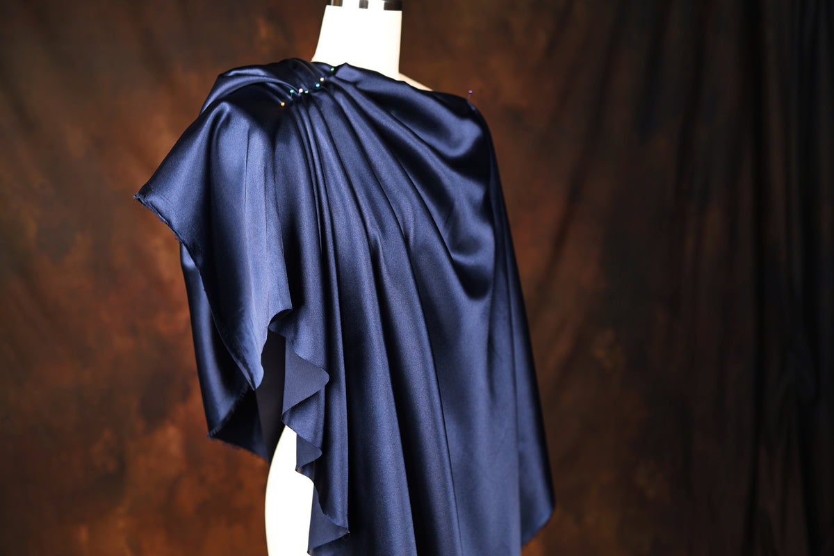 A mannequin wearing a blue satin cape with a draped, flowing design.