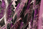 The image is a close-up of a fabric with a floral pattern in shades of purple and black, adorned with gold sequins.