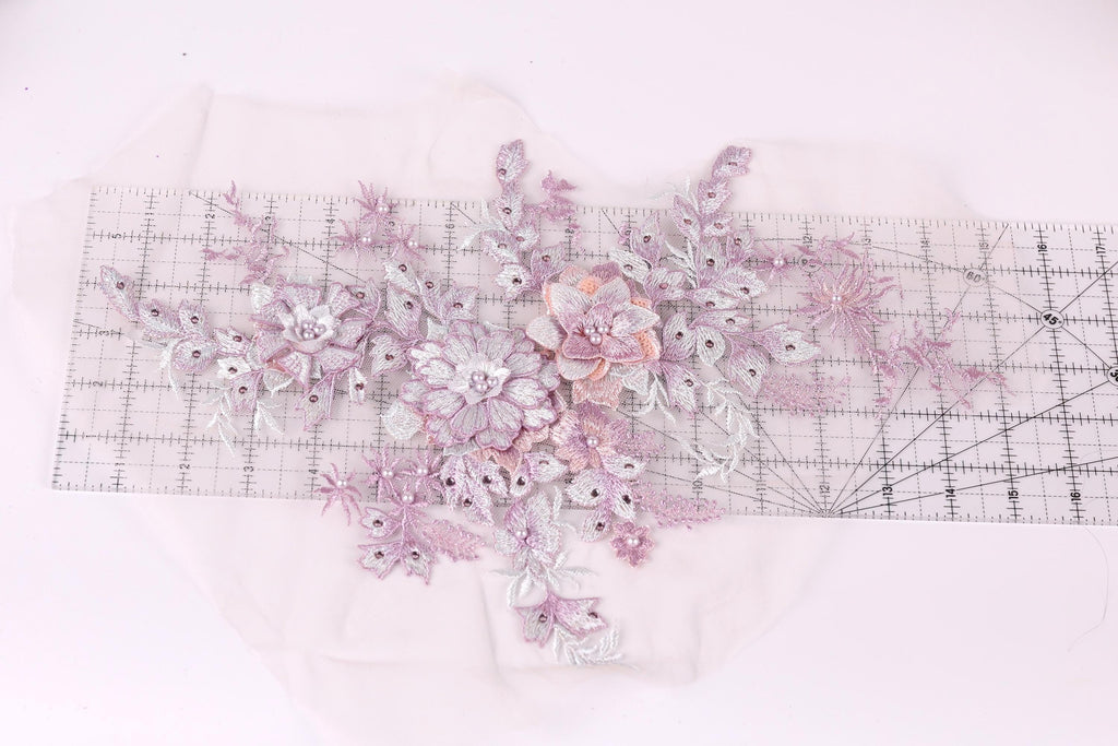 a close-up view of a delicate floral embroidery piece, showcasing a variety of pink and white flowers and leaves. The intricate details and vibrant colors of the embroidery create a visually appealing and artistic composition.