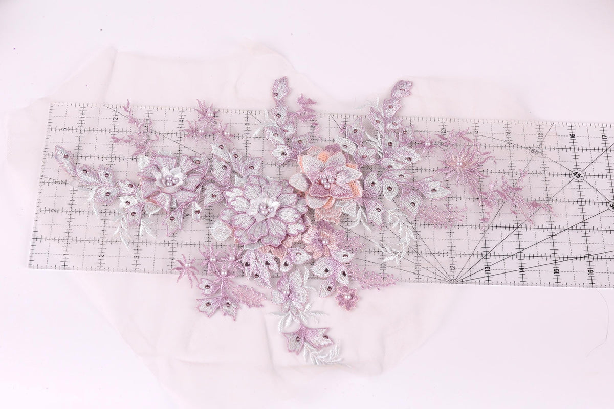 a close-up view of a delicate floral embroidery piece, showcasing a variety of pink and white flowers and leaves. The intricate details and vibrant colors of the embroidery create a visually appealing and artistic composition.