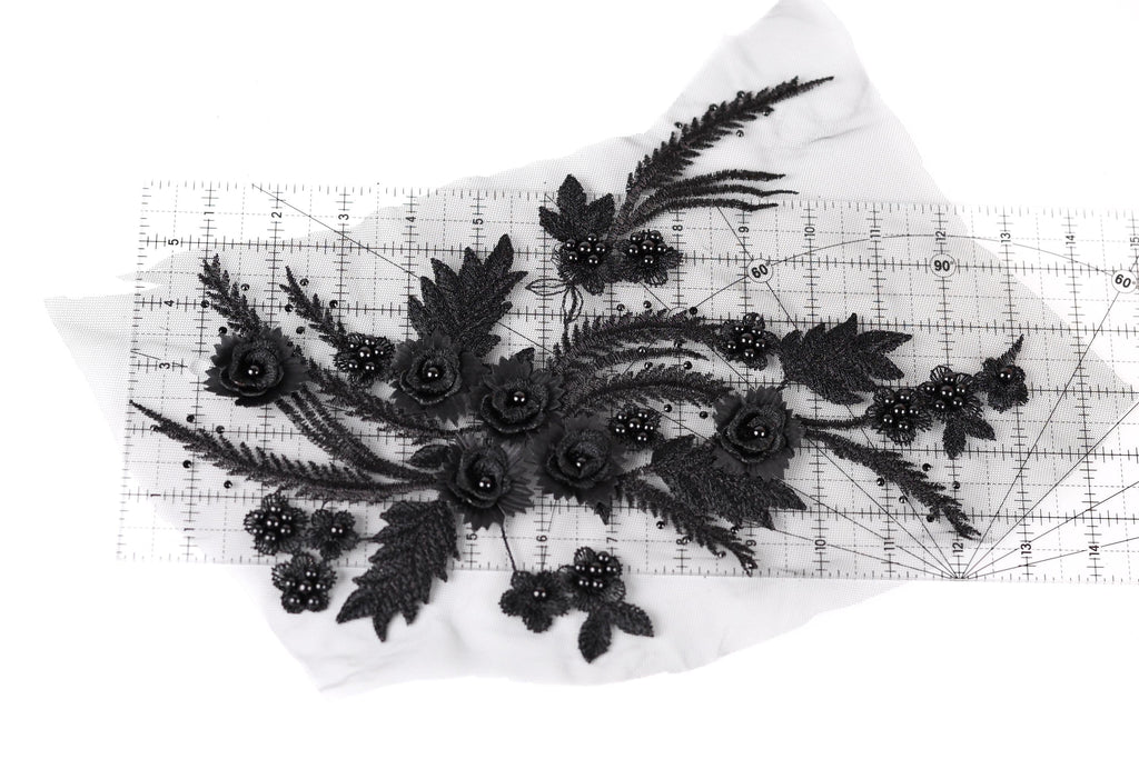 a close-up view of a black lace flower design with numerous black beads and leaves attached to it.