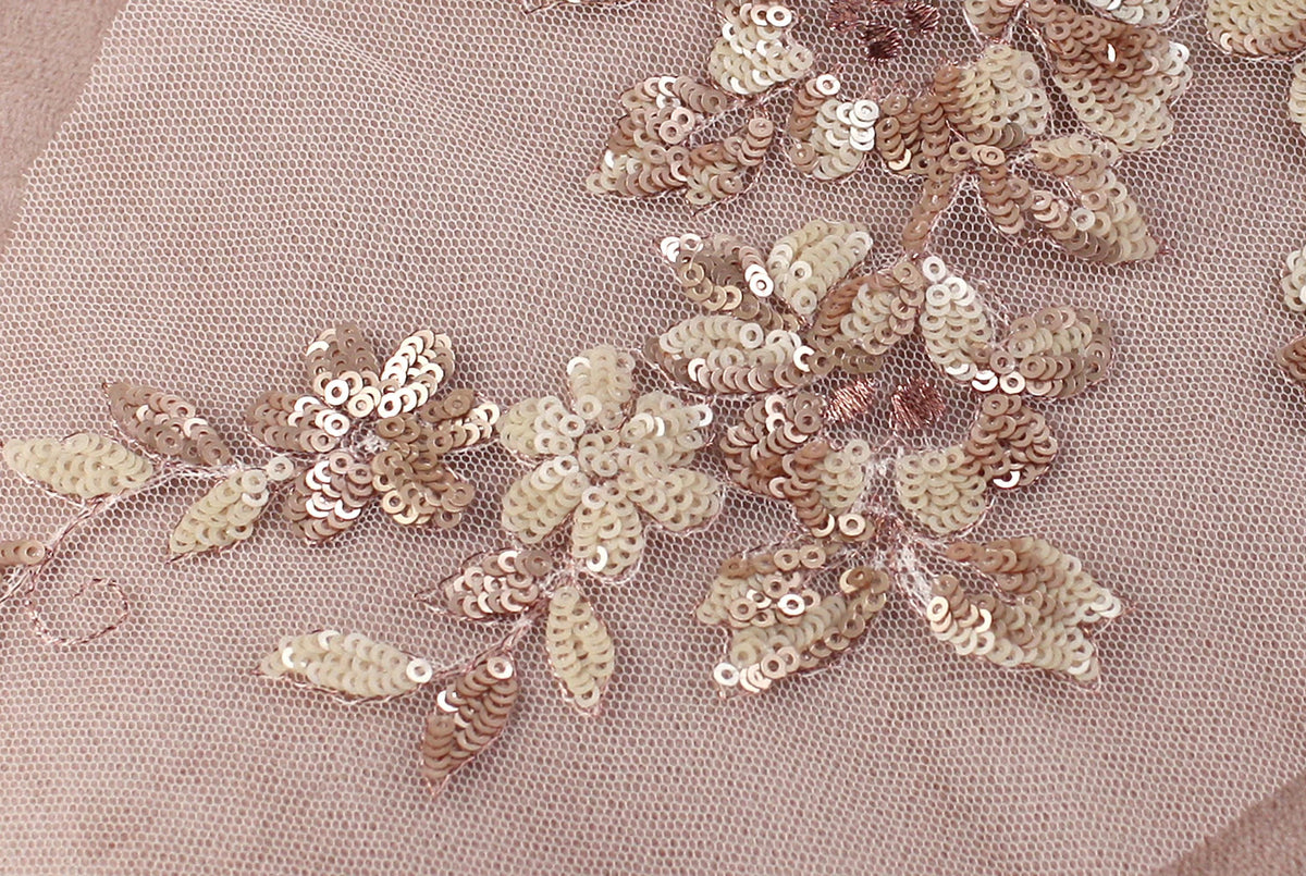 a close-up view of a delicate, intricate piece of fabric adorned with a floral pattern made of small, round, beige and brown sequins.