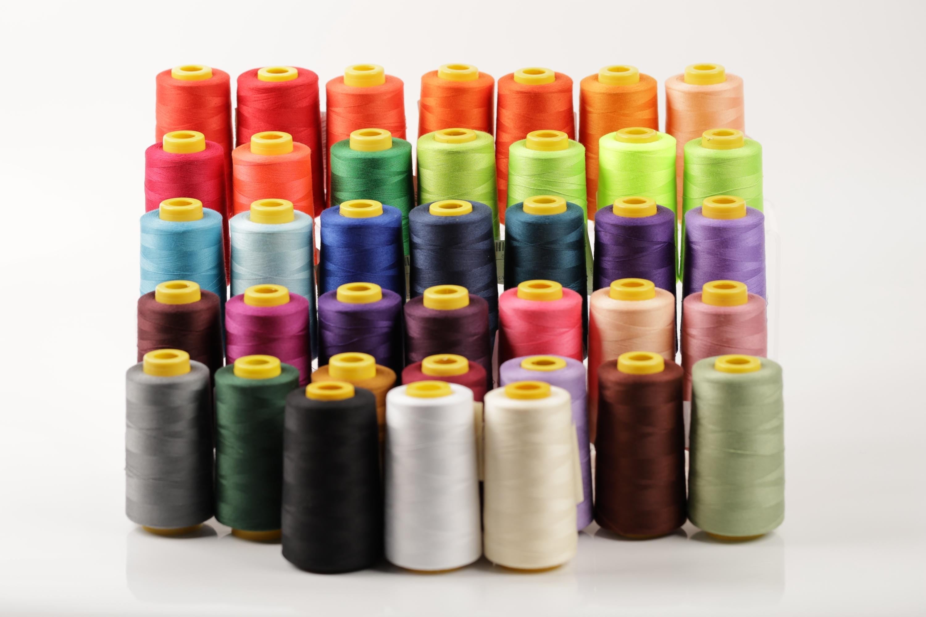 A collection of colorful spools of thread arranged in rows on a white background.
