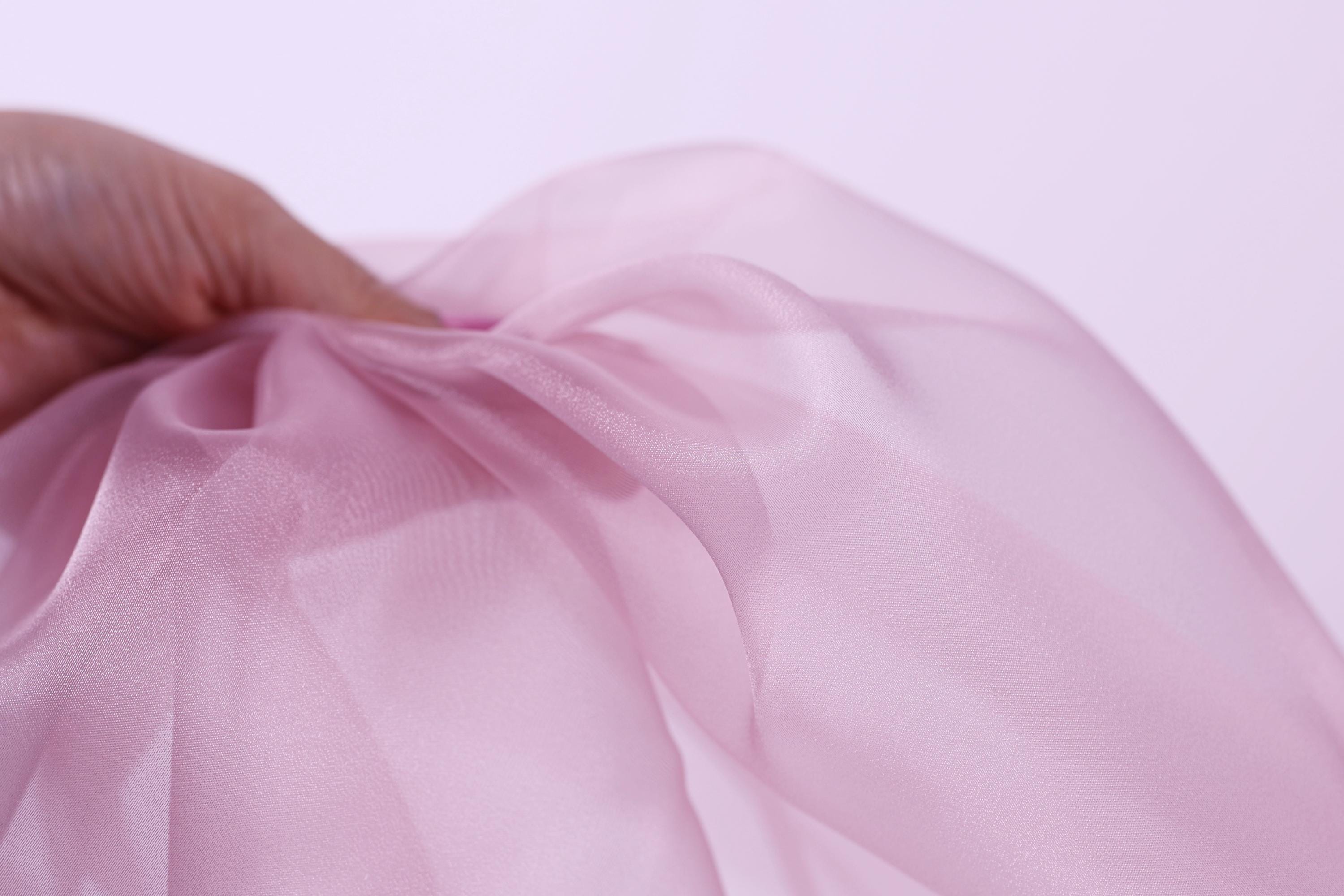 A hand is holding a piece of pink fabric, which appears to be a soft, flowing material.