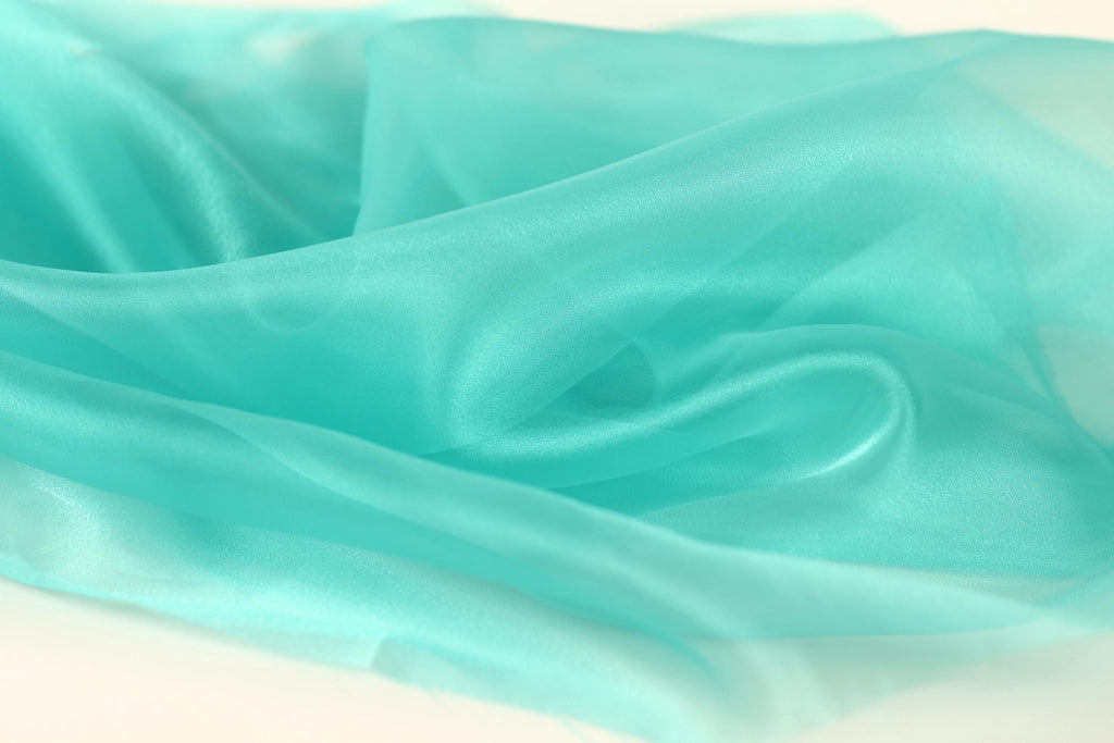 a close-up view of a light blue, turquoise-colored fabric, possibly silk or chiffon, with a soft, flowing texture.